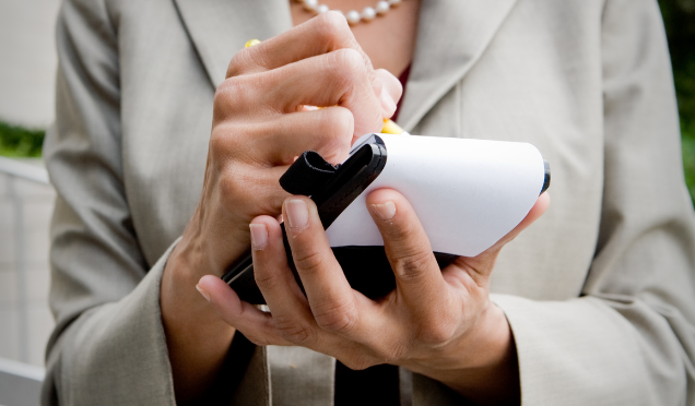 Person holding a handheld device while pressing a button, dressed in a business jacket.
